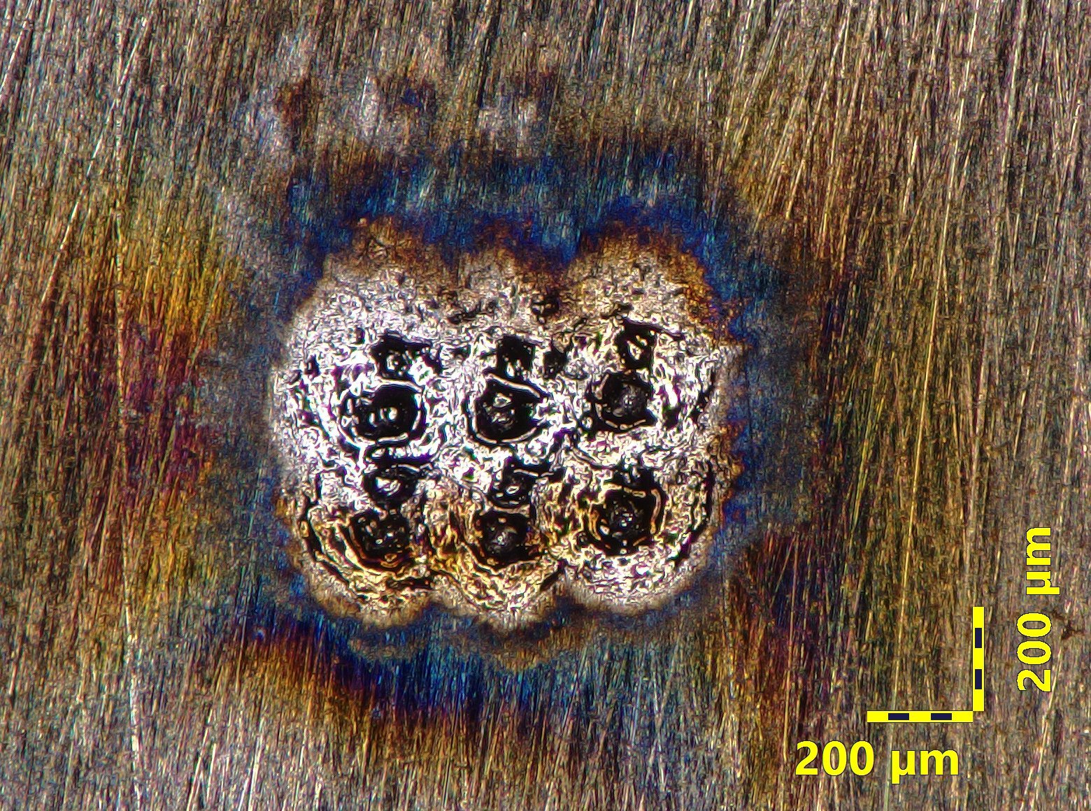 True-color micrograph of LIBS burn marks on gray iron at 160x, showing heat tint and crater morphology